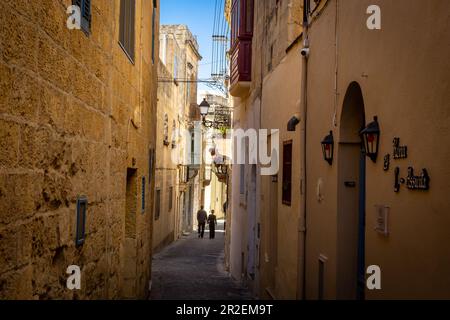 Rabat, Gozo, Malta - 18. April 2023: Ein Paar, das in einer engen Straße mit historischer Architektur spaziert. Stockfoto