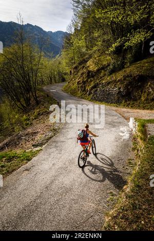 Junge Frau fährt mit dem Mountainbike eine enge Asphaltstraße hinauf, Idro-See, Italien Stockfoto