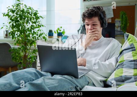 Verärgerter junger Kerl zu Hause, der auf ein Notebook schaut Stockfoto