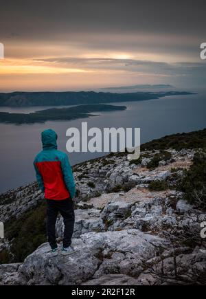 Mann, der die Insel Hvar vom Aussichtspunkt Vidova Gora auf Brac bei Sonnenuntergang, Kroatien, betrachtet Stockfoto