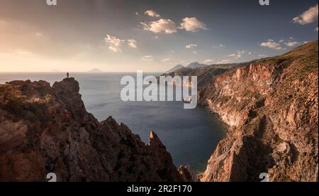 Ein Mann auf einer Klippe an der felsigen Lipari Küste bei Sonnenuntergang, Sizilien Italien Stockfoto