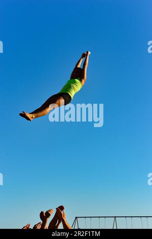 Eine junge Frau wird von ihren Freunden in die Luft geworfen und macht Akrobatik am Santa Monica Beach, Kalifornien, USA Stockfoto