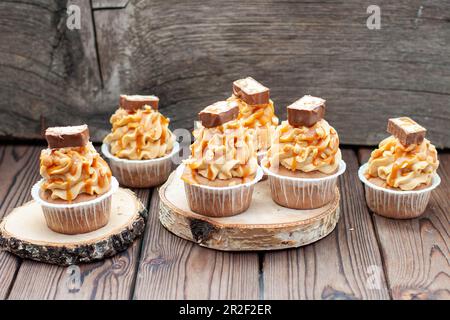 Köstliche Schokoladen-Cupcakes mit Erdnussbutter-Zuckerguss, Schokoladensauce und gesalzener Karamellsauce auf rustikalem Holzhintergrund Stockfoto