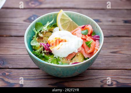 Brunch mit pochiertem Ei, Avocado, Rucola, Leinsamen und gesalzenem Lachs auf rustikalem Holzhintergrund. Flach, horizontal. Speicherplatz kopieren Stockfoto