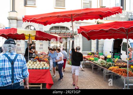 Der junge Mann trägt einen Sonnenschirm durch die Marktstände vor der Markthalle, Les Halles, Redon, Ille-et-Vilaine, Bretagne, Frankreich, Euro Stockfoto