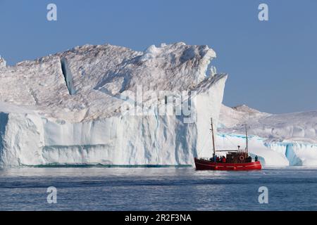 Disco Bay in Westgrönland; Eisberge im Kangia Icefjord bei Ilulissat; rotes Tourboot mit Besuchern nähert sich einem Eisberg; steile Mauern und Demoli Stockfoto