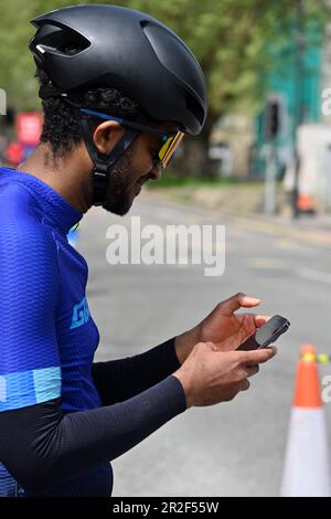 Männlicher Radfahrer mit Sonnenbrille und Helm, der auf das Handy schaut, wenn er vom Fahrrad abfährt Stockfoto