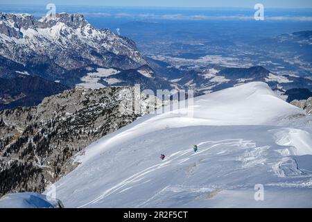 Zwei Personen auf einer Skitour steigen eine Schneeflanke hinab, Untersberg im Hintergrund, Hohes Brett, Berchtesgaden-Nationalpark, Berchtesgaden-Alpen, Oberbayern Stockfoto