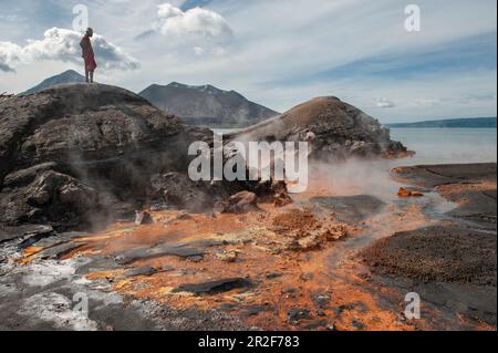 Ein junger Mann steht auf Felsen und schaut auf Orangenrückstände und heiße Quellen in der Nähe eines aktiven Vulkans, Rabaul, East New Britain Province, Papua-Neuguinea, S. Stockfoto