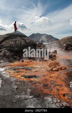 Ein junger Mann steht auf Felsen und schaut auf Orangenrückstände und heiße Quellen in der Nähe eines aktiven Vulkans, Rabaul, East New Britain Province, Papua-Neuguinea, S. Stockfoto