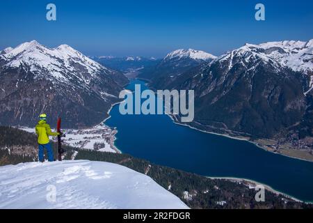 Snowboarder mit Splitboard im tiefen Schnee und Blick auf den Achensee und die Berge im Frühling mit Schnee Stockfoto