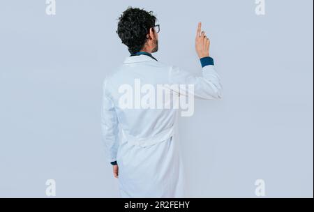Doktor posiert mit dem rückwärtigen Finger. Junger Arzt aus rückenzeigendem Finger isoliert Stockfoto