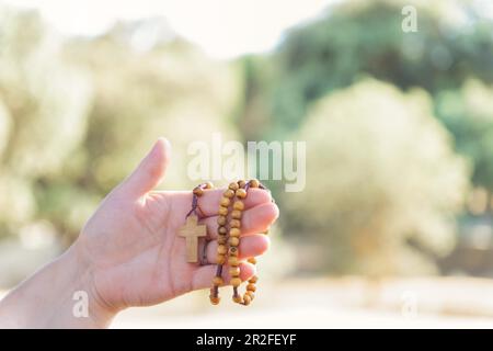 Frauenhände halten einen christlichen Rosenkranz mit einem Kreuz, beten in der Dämmerung auf einem Feld Stockfoto