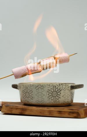 Marshmallows spießen im Feuer einer Keramikschüssel auf einem Holzbrett auf Stockfoto