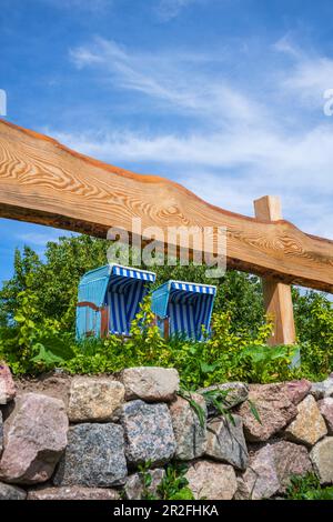 Zwei blaue weiße Liegestühle im Garten hinter einem Holzzaun mit einer Steinmauer und blauem Sommerhimmel, Usedom, Mecklenburg-Vorpommern, Deutschland Stockfoto