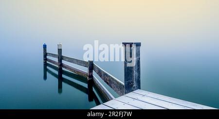 Schneebedeckte Anlegestelle im Jachthafen bei nebeligem Sonnenaufgang am Starnberger See, Seeshaupt, Bayern, Deutschland Stockfoto