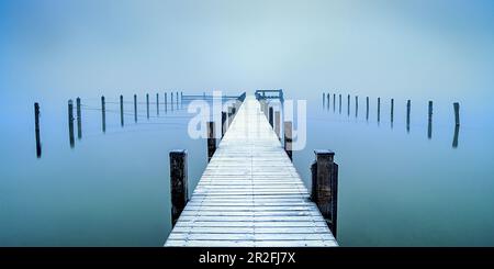 Schneebedeckte Anlegestelle im Jachthafen bei nebeligem Sonnenaufgang am Starnberger See, Seeshaupt, Bayern, Deutschland Stockfoto