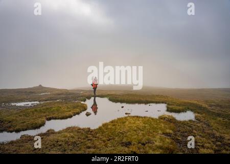 Wanderer stehen auf einer spiegelglatten Wasseroberfläche im Hochmoor der Klakkur, Klaksvík und Färöer Inseln. Stockfoto