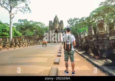 Ein junger Mann mit Rucksack fotografiert den Eingang zum Bayon-Tempel Angkor Thom Tor. Siem Reap, Kambodscha Stockfoto