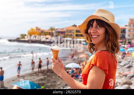 Im Sommer lächelt eine touristische Frau mit einem Hut und isst ein Eis am Strand am Valle Gran Rey auf La Gomera, Kanarische Inseln Stockfoto