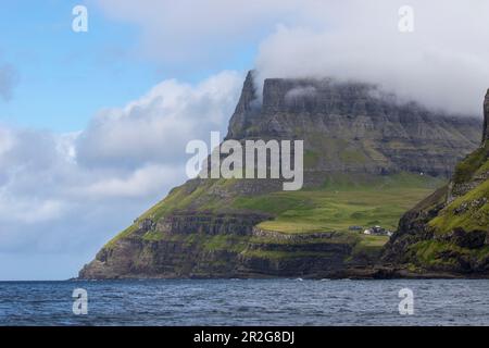 Ein paar kleine Häuser auf einer Klippe vor einer Bergkulisse. Gasadalur, Vagar, Färöer. Stockfoto