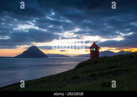 Kleiner roter Leuchtturm an einer grünen Küste. Berg im Meer. Velbastadur, Streymoy, Färöer. Stockfoto