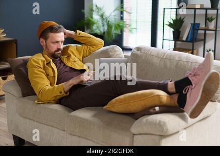 Ein kluger Programmierer, der sich Gedanken darüber macht, wie man Programmcode schreibt. Freiberufler, die bequem auf dem Sofa liegen und von zu Hause aus arbeiten, profitieren von Flexibilität und den Vorteilen der Fernarbeit. . Hochwertiges Foto Stockfoto