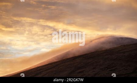 Wolken sammeln sich über dem Mount Cruach Mhartain bei Sonnenaufgang. Goldenes Licht. Clogher, Dnurlin, County Kerry, Irland. Stockfoto