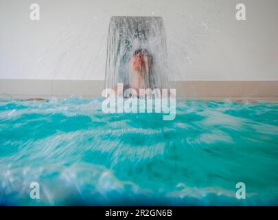 Frau im Hydro Massagepool mit fallendem Wasser im Swimmingpool in der Schweiz. Stockfoto