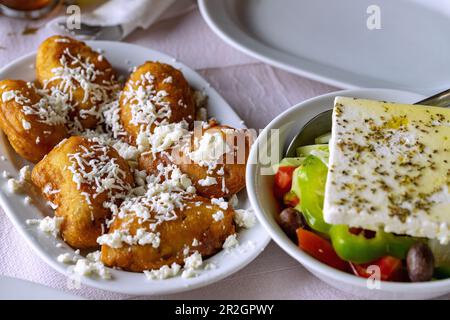 Louloudia/Anthous gemista, Zucchini-Blumen gefüllt mit Fetakäse, mariniert in Ei und sautiert mit griechischem Farmer-Salat, serviert in Taveren Sprotte Stockfoto