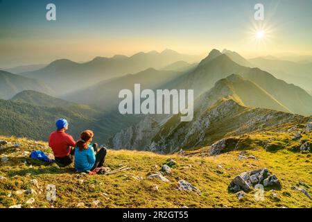 Mann und Frau, die auf dem Gipfel sitzen und über die Karawanken, Veliki vrh, Hochturm, Karawanken, Slowenien, Kärnten, Österreich Stockfoto