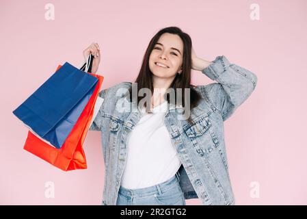 Joyful Shopper: Young Woman in Denim Shirt feiert, Arm Elevated in Enthusiasmus, Against Pink Background, enthusiastisch von Online Shopping oder Amazing Stockfoto