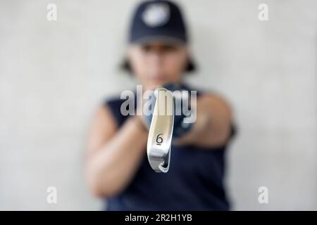 Golfer mit Cap hält ihren Iron Golf Club 6 mit ihrem Golfhandschuh an einem sonnigen Tag in der Schweiz. Stockfoto