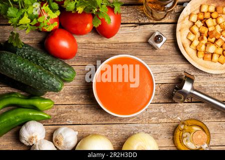 Gemüse brauchte man, um eine Gazpacho um eine Schüssel gefüllt mit Gazpacho und Stückchen getoastetes Brot auf einem rustikalen Holztisch zu machen. Stockfoto