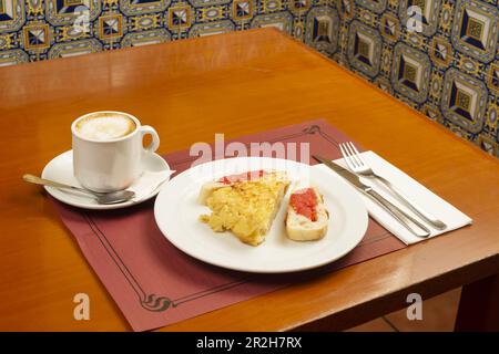 Ein typisches spanisches Frühstück mit Tortilla-Spieß mit Scheiben Pan con Tomate und Kaffee mit Milch in einer Tasse auf einem Holztisch Stockfoto