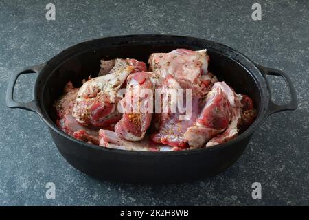 Gewürztes Lammfleisch in schwarzem Eisentopf, zum Braten bereit, auf dunklem Steinhintergrund, Seitenansicht Stockfoto