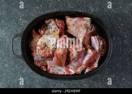 Gewürztes Lammfleisch in schwarzem Eisentopf, zum Braten bereit, auf dunklem Steinhintergrund, Draufsicht Stockfoto
