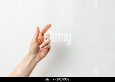 Weibliche Hand mit pastellrosa Nagellack und goldenem Ring am Finger isoliert auf weißem Hintergrund Stockfoto