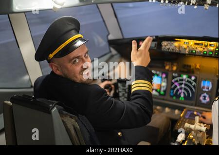 Kaukasischer bärtiger Mann, der beim Fahren eines Flugsimulators lächelt. Der Pilot im Cockpit zeigt Daumen nach oben. Stockfoto