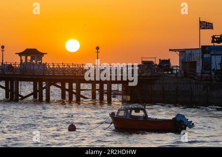 Der Himmel leuchtet orange während des Sonnenaufgangs über dem Pier in Swanage in Dorset. Stockfoto