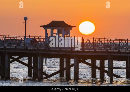 Der Himmel leuchtet orange während des Sonnenaufgangs über dem Pier in Swanage in Dorset. Stockfoto