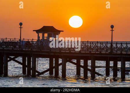 Der Himmel leuchtet orange während des Sonnenaufgangs über dem Pier in Swanage in Dorset. Stockfoto