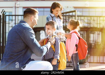 Junge Eltern sagen ihren kleinen Kindern in der Nähe der Schule Auf Wiedersehen Stockfoto