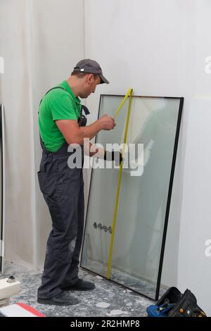 Arbeiter bei der einheitlichen Messung von Doppelverglasungsfenstern im Innenbereich Stockfoto