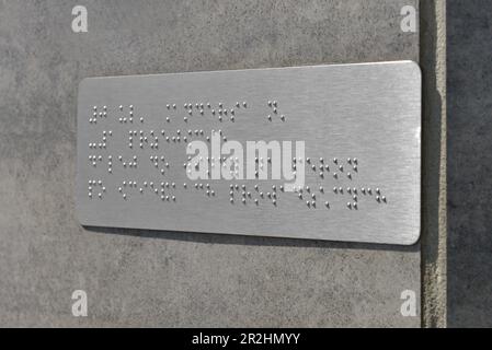 Silberplatte mit Braille-Text an grauer Wand, Nahaufnahme Stockfoto