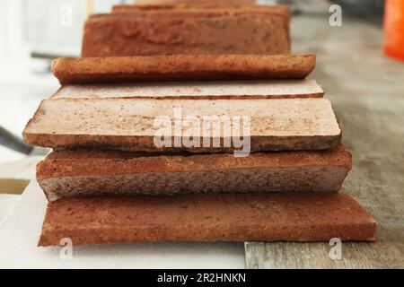 Viele dekorative Ziegel auf Gerüsten, Nahaufnahme. Installationsvorgang für Fliesen Stockfoto