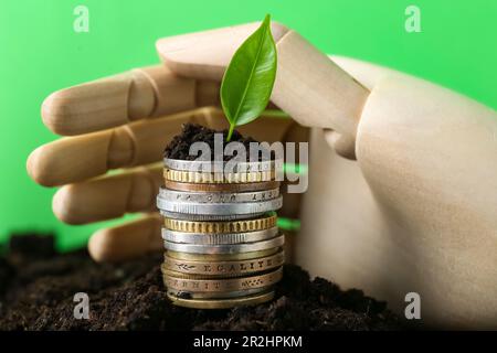 Münzstapel, grüne Pflanze und hölzerne Schaufensterhand auf dem Boden vor verschwommenem Hintergrund. Gewinnkonzept Stockfoto