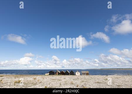 Eine Reihe einsamer Fischerhütten stehen am Steinstrand. Grausige Wolken und blauer Himmel. Die Helgumannen-Fischerei. Faroe, Grafschaft Gotland, Schweden. Stockfoto