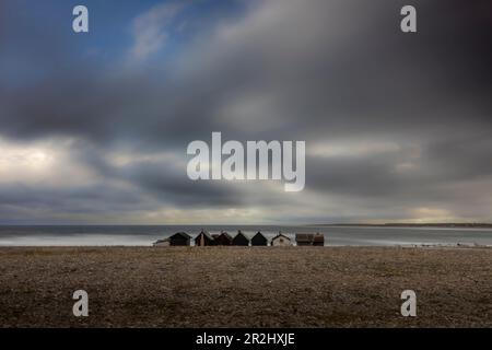 Eine Reihe einsamer Fischerhütten stehen am Steinstrand. Bedrohliche Wolken am Himmel. Die Helgumannen-Fischerei. Faroe, Grafschaft Gotland, Schweden. Stockfoto