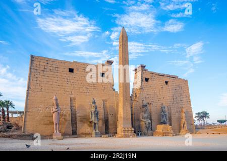 Der Pylon von Ramessa II mit dem östlichen Obelisken und den beiden Kolossen des Königs, die auf seinem Thron, dem Tempel von Luxor, Luxor, Theben, UNESCO sitzen Stockfoto